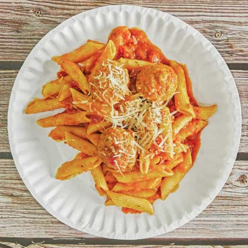 Penne pasta with meatballs and tomato sauce, topped with shredded cheese on a white plate.
