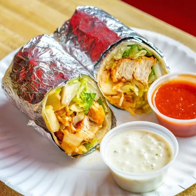 Two chicken wraps, partially unwrapped from foil, with side cups of red and white sauces.